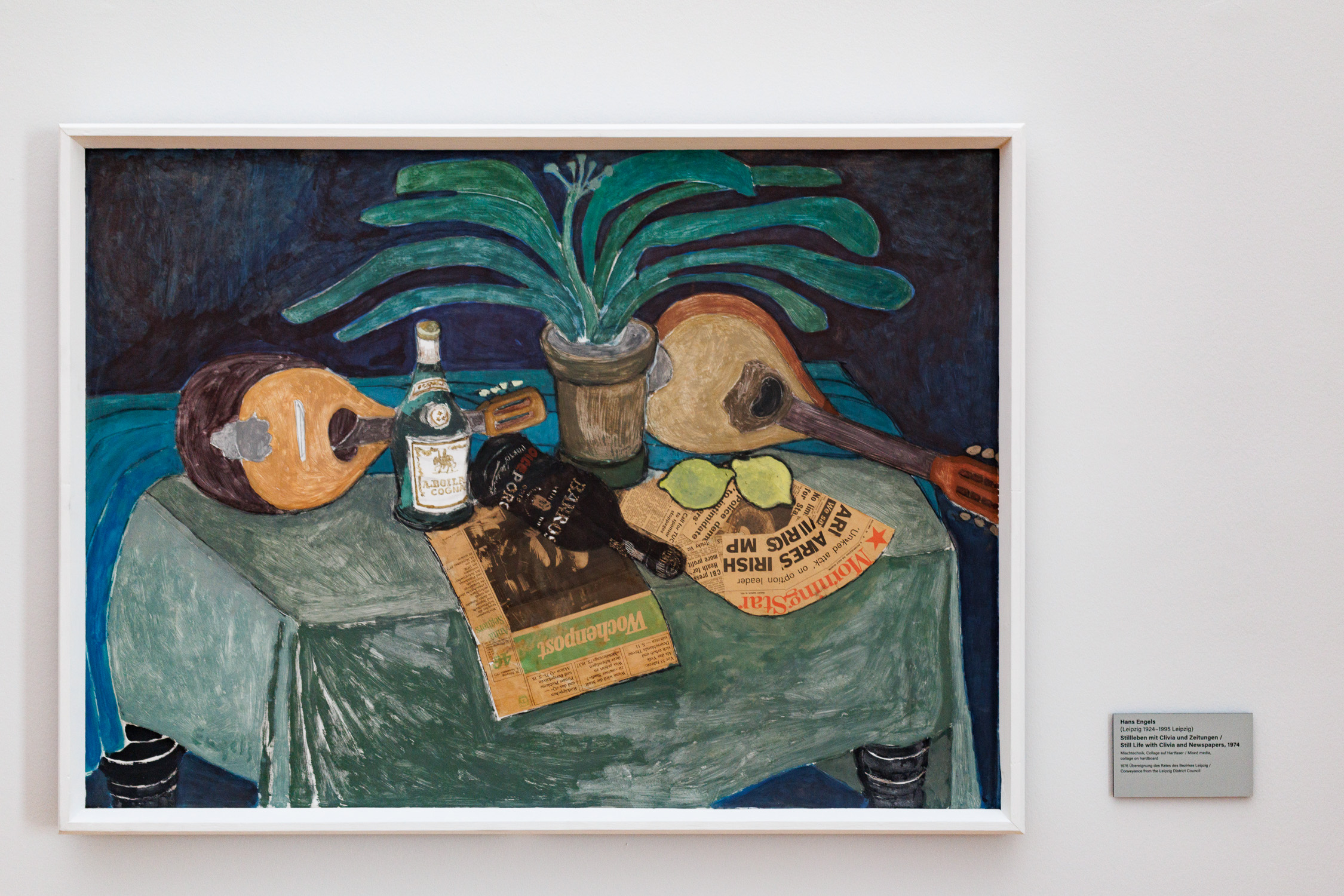 A still life with musical instruments, bottle and plant painted. Real newspaper clippings are embedded within the painting as elements of the still life.